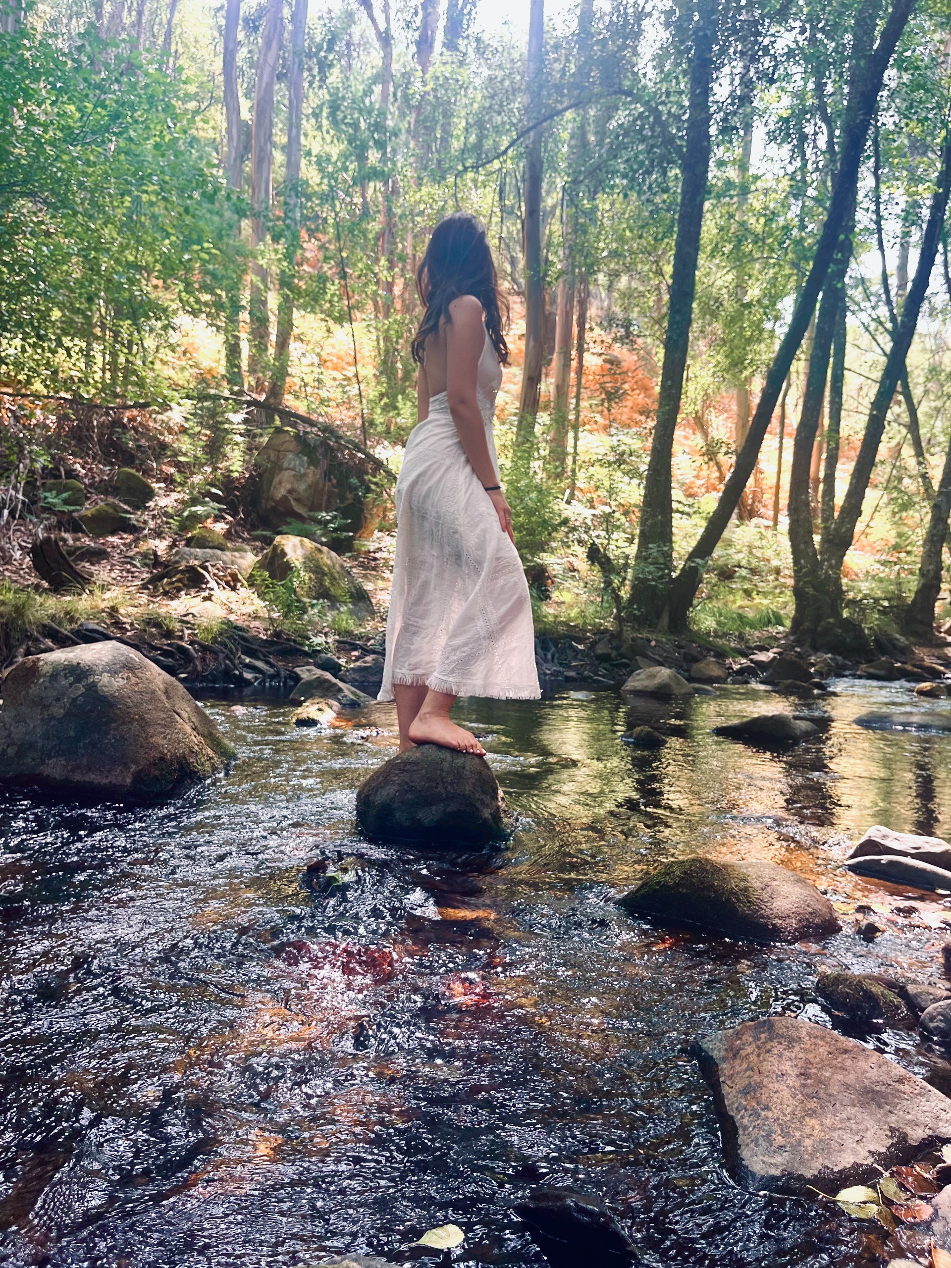 Agathe standing barefoot on river rocks in a sunlit forest